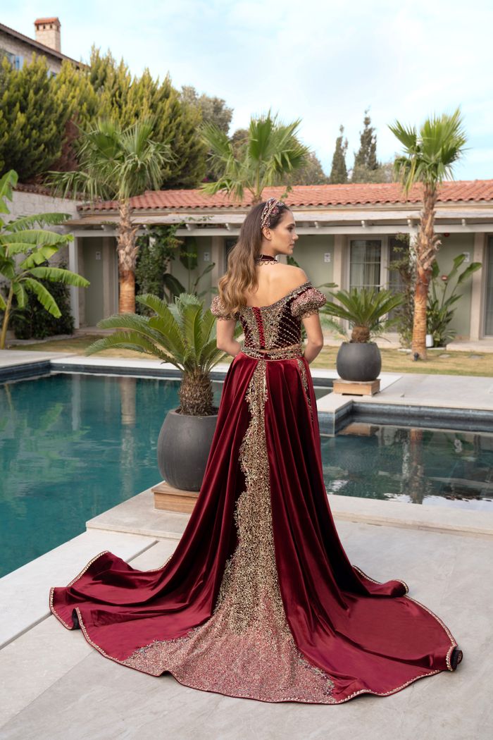 A luxurious red evening gown with intricate detailing, modeled outdoors by a poolside in Izmir, Turkey.