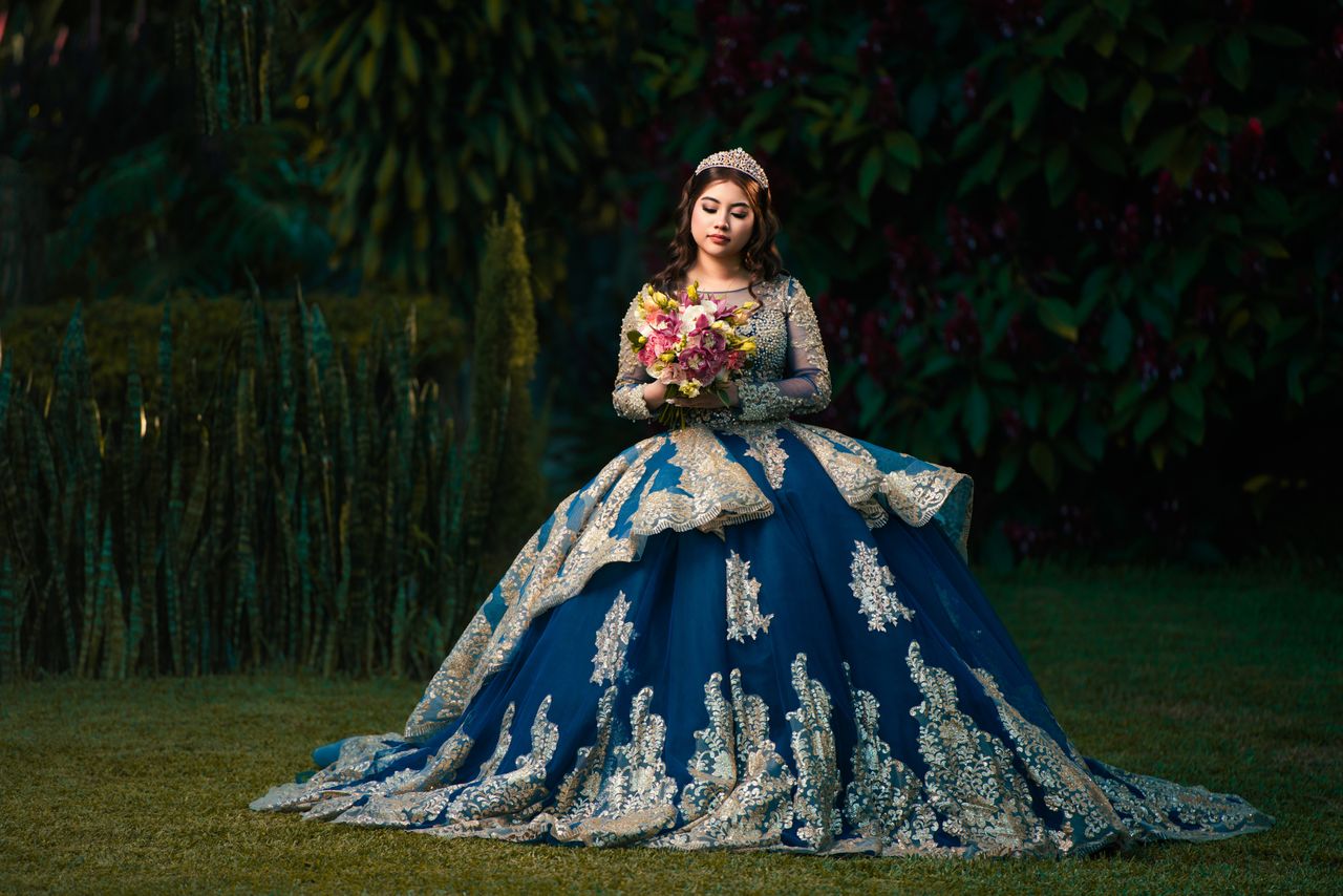 A woman in a stunning blue gown holds flowers in a lush garden setting. Perfect for fairytale and formal themes.
