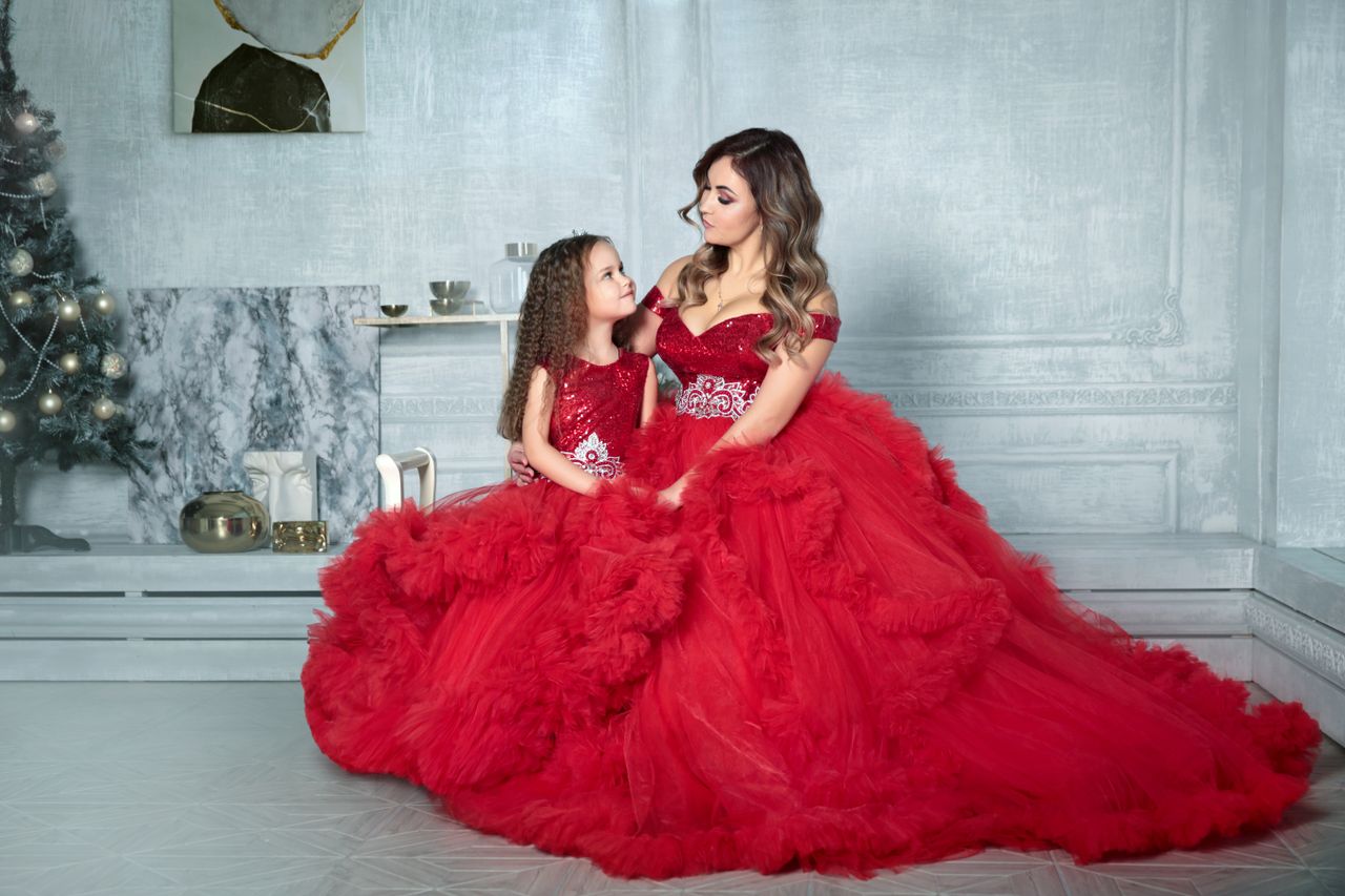 Mother and daughter in matching red gowns posing elegantly in a festive indoor setting.